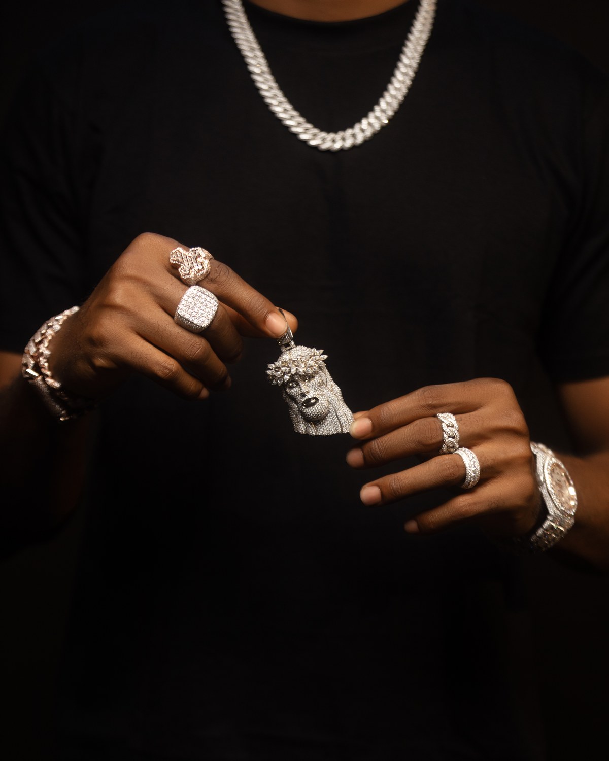 Hands presenting a diamond face pendant with rings, a bracelet, and a watch.