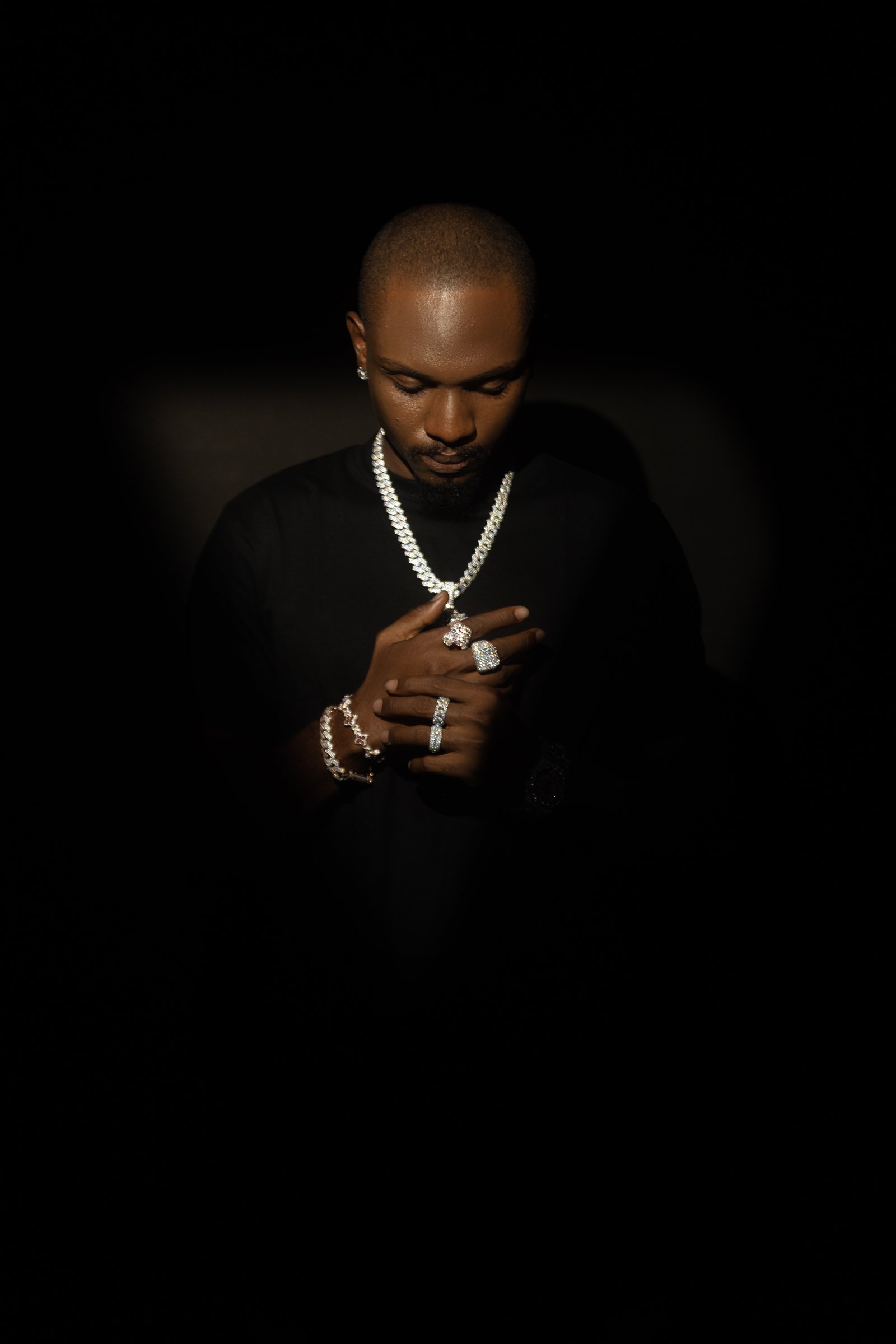 Model looking down while wearing layered diamond jewelry against a black background.